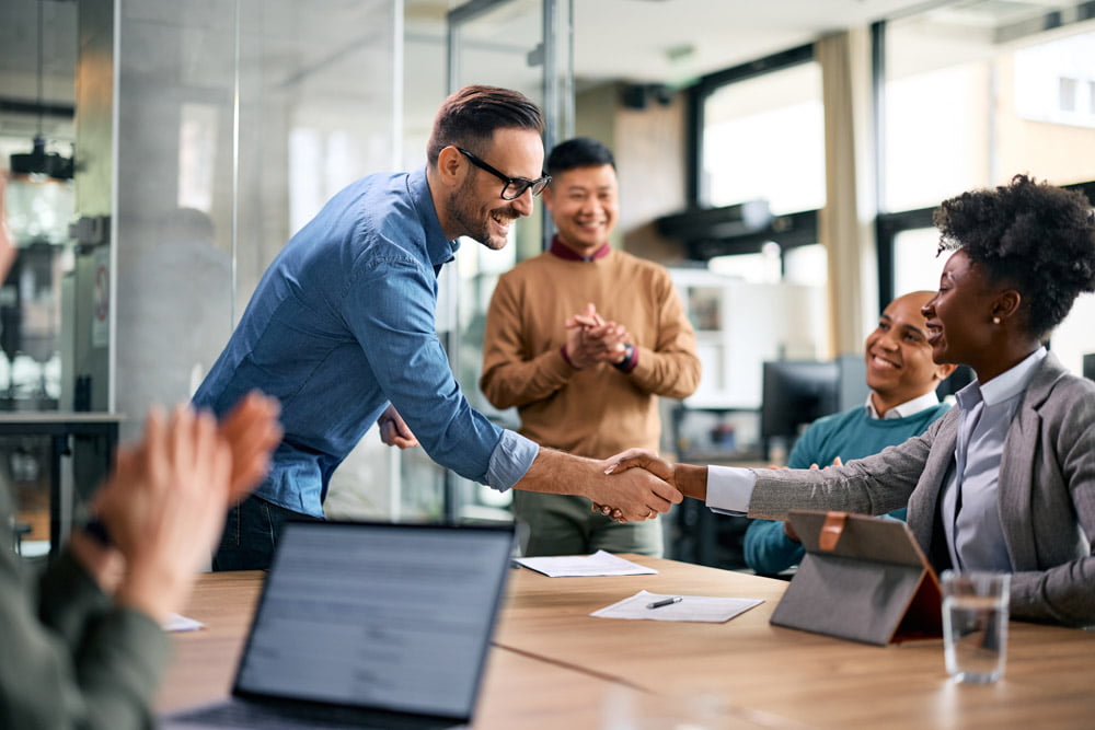 Happy CEO handshaking with black female colleague during business meeting in office.